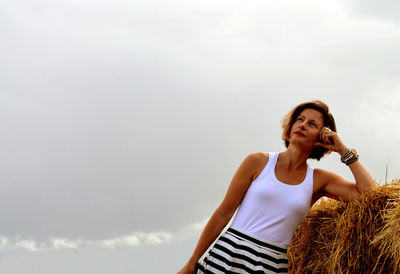Thoughtful woman leaning on hay against sky