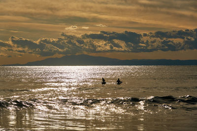 Silhouette swimming in sea against sky during sunset