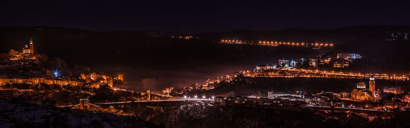 Illuminated cityscape by river against sky at night