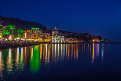 Illuminated buildings by river against sky at night