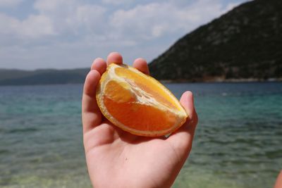 Close-up of hand holding orange against river