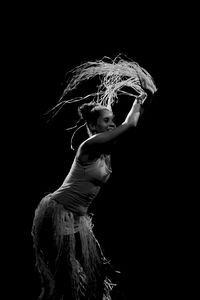 Contemporary dancer dancing in theater with black background and straw accessory. 