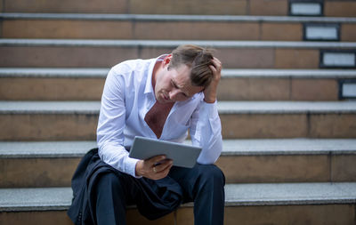 Full length of man using mobile phone while sitting on staircase