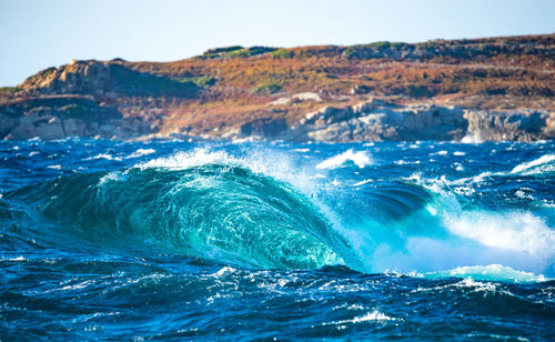 Sea waves splashing on shore against sky