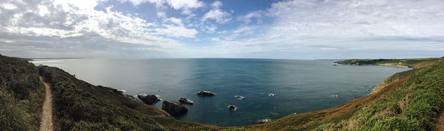 Panoramic view of mountains with rocks by sea against cloudy sky