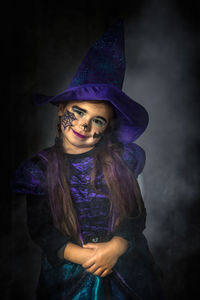 Portrait of young woman standing against black background