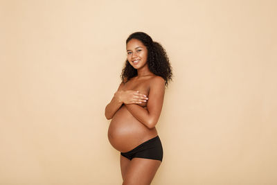 Portrait of shirtless pregnant woman against beige background