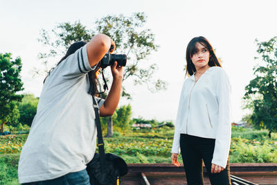 Young woman photographing with camera while standing against sky