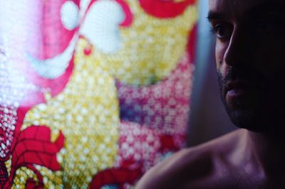 Close-up of shirtless man looking away against patterned curtain