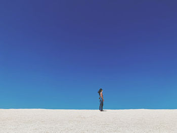 Side view of man standing on desert against clear blue sky