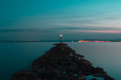 Illuminated lighthouse by sea against blue sky at dusk