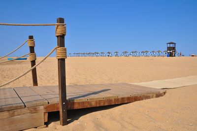 Wooden posts on beach against clear blue sky