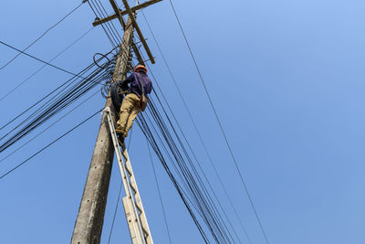 Low angle view of electrician repairing power lines against clear sky