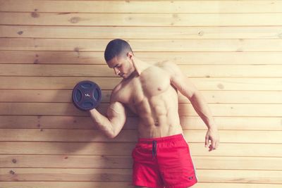 Shirtless man exercising against wooden wall