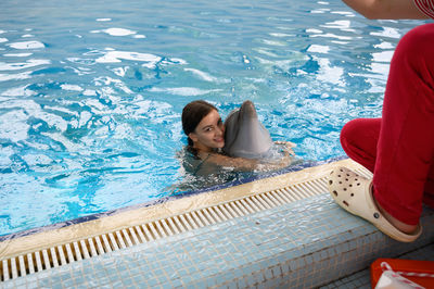 Man crouching by woman with dolphin in swimming pool