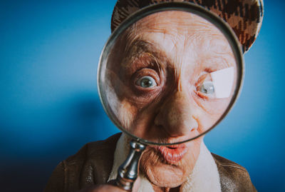 Close-up portrait of senior man looking through magnifying glass against blue background