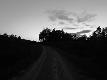 Road amidst silhouette trees against sky