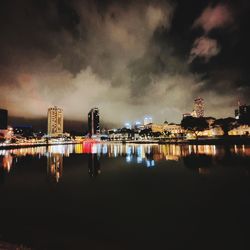 Illuminated buildings by river against sky at night