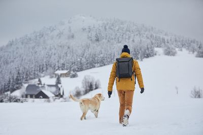 Rear view of man walking with dog on snow covered land