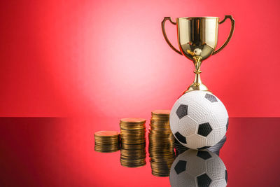 Close-up of coins with trophy and soccer ball against red background
