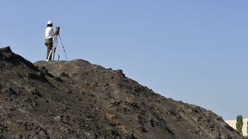 Low angle view of woman standing on rock against clear sky