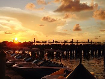 Sailboats moored on harbor in city against sky during sunset