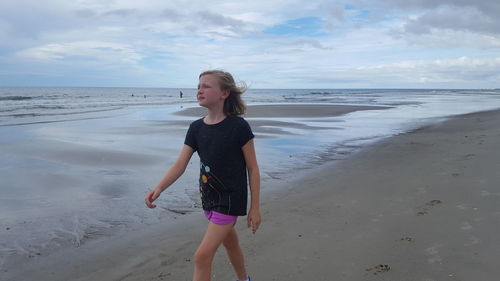 Teenage girl walking on beach against sky