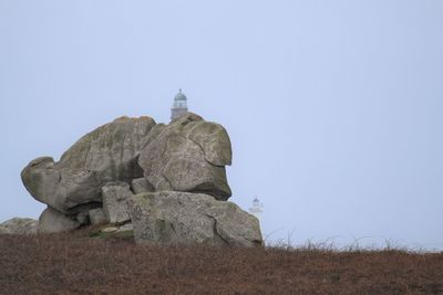 Low angle view of  lighthouse behind rocks against clear sky