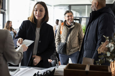 Businesswoman taking id card from receptionist at registering counter in convention center