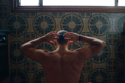 Rear view of muscular shirtless man standing against wall