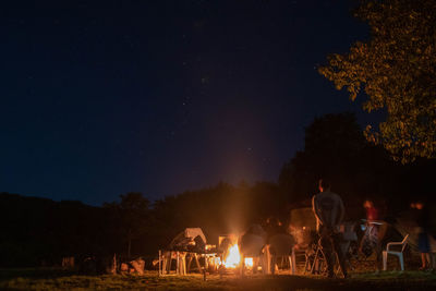 People sitting on field against trees at night