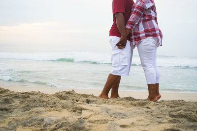 Low section of couple standing at beach against sky