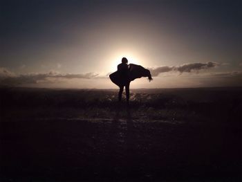 Silhouette of woman standing on landscape at sunset