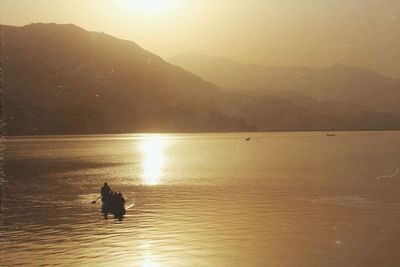 Silhouette swans swimming on lake against sky during sunset