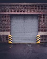 Empty road against shutter in brick wall