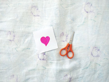 Directly above shot of paper with pink heart shape by scissors on bed