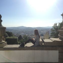 Woman sitting on rock against sky