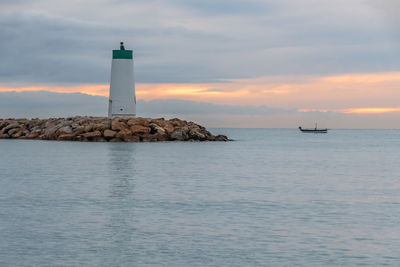 Lighthouse amidst sea and buildings against sky