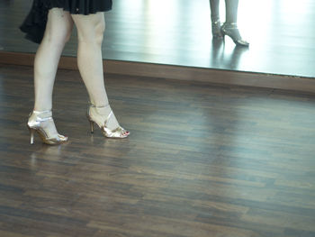 Low section of woman in high heels standing on hardwood floor