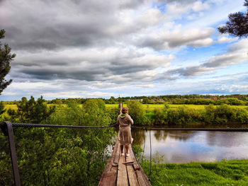 Rear view of woman standing by lake against sky