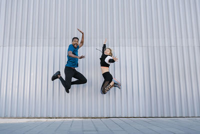 Full length of young woman jumping against wall