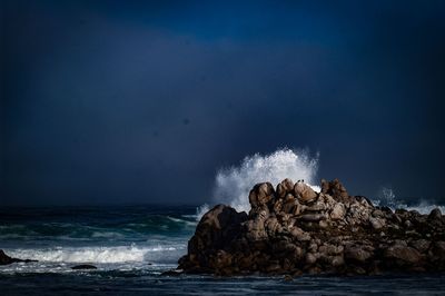 Waves breaking against rocks in sea against sky