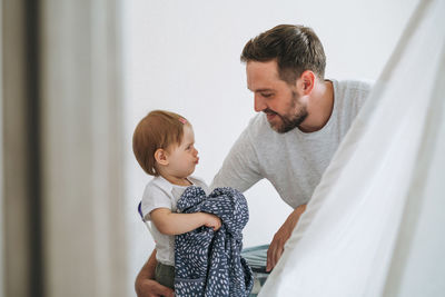 Father young man and crying upset baby girl little daughter in children room at home