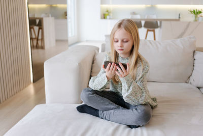 Portrait of young woman using mobile phone while sitting on bed at home