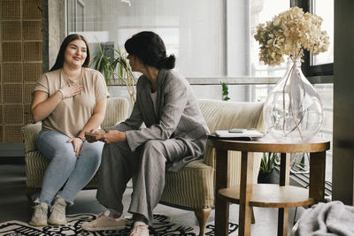 Smiling non-binary professional discussing with businesswoman while sitting at office