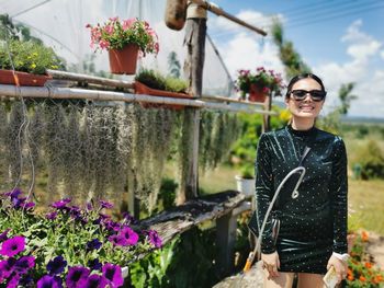 Young woman wearing sunglasses standing by flower plants