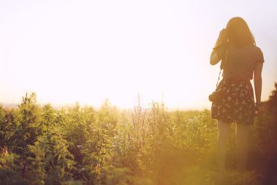 Rear view of woman standing on field against clear sky during sunset