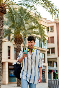 Young man using smart phone while standing on palm tree