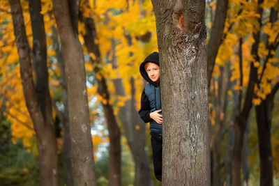 Portrait of cute boy hiding behind tree