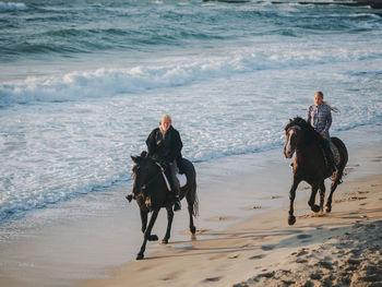 Friends horseback riding on shore at beach